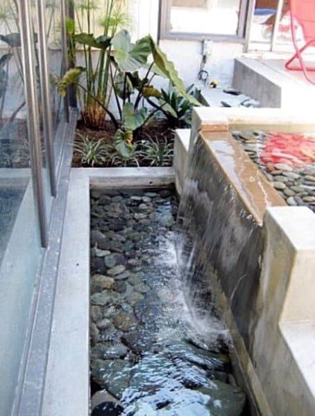 Modern concrete-raised waterfall pond with smooth stones and lush plants.