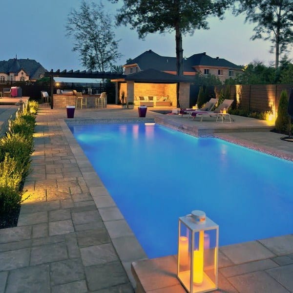 Modern backyard with illuminated swimming pool, lounge chairs, and ambient lantern lighting.