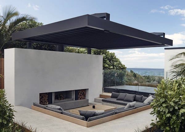 Modern backyard with a sunken seating area, sleek fireplace, and pergola overlooking the ocean.