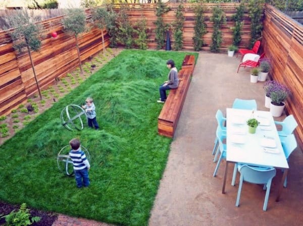 Playful backyard with grassy hills, wooden seating, dining area, and modern wooden fencing.