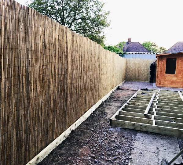 Tall bamboo reed privacy fence alongside a wooden deck frame in a backyard.