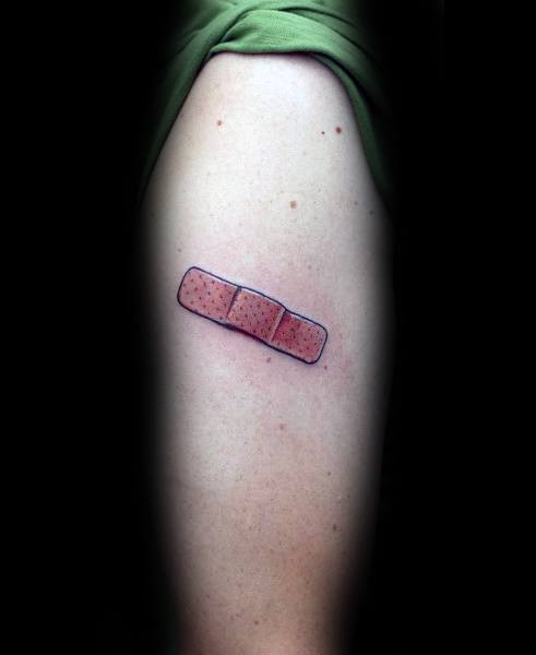 Small and realistic Band-Aid tattoo with light bruising effect, placed on the upper arm for a subtle, healing-inspired look.