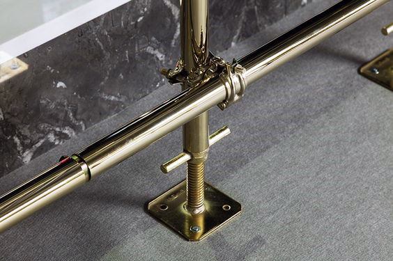 Gold-plated metal foot rail with sturdy support brackets attached to a marble bar on a carpeted floor.