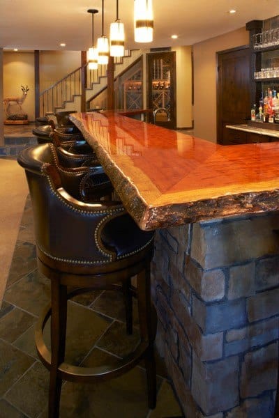 Glossy live edge wood bar top with leather bar stools and stone base.