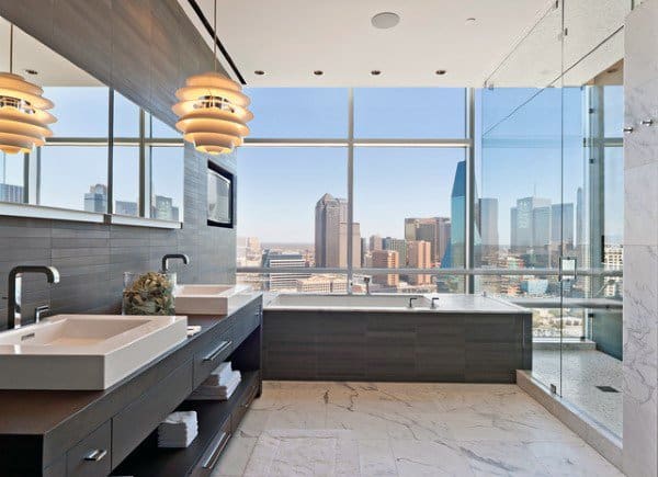 Modern bathroom with seamless mirror, double sinks, and floor-to-ceiling city view windows.