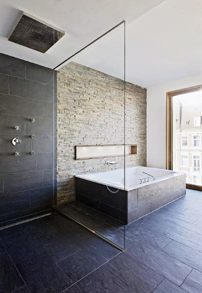 Modern bathroom with a glass shower, stone wall, and sunken bathtub by a window