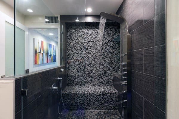 Modern bathroom with a sleek black pebble tile shower and bench, featuring a unique waterfall-style shower