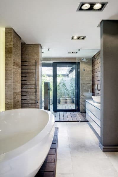 Modern bathroom with a large tub, double sinks, and glass door leading outside