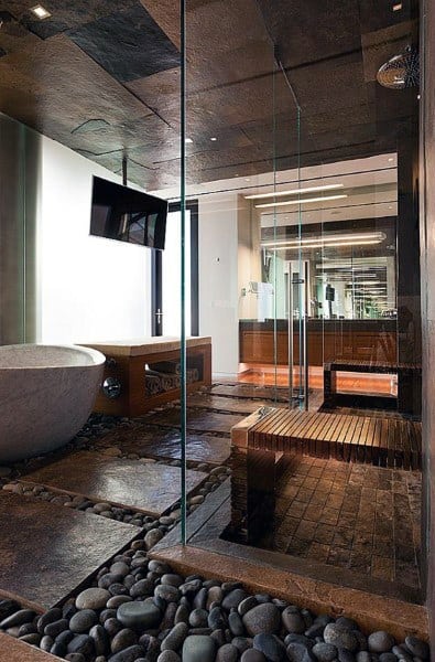 Modern bathroom with stone bathtub, glass shower, wooden bench, and pebbled floor