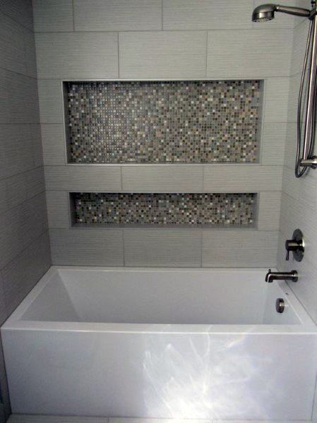 White bathtub with recessed mosaic tile shelves and gray wall tiles in modern bathroom.