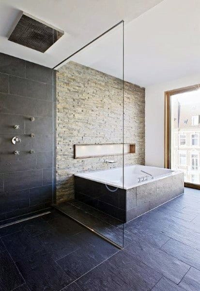 Modern bathroom with natural stone brick accent wall, built-in tub, and glass shower partition.
