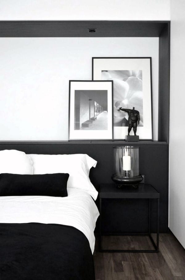Modern black and white bedroom with framed art, black bedding, and minimalist side table.