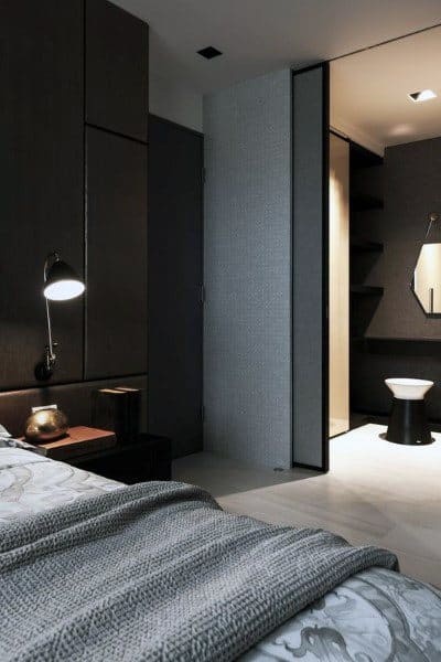 Cozy bedroom with dark walls, modern lighting, and an open view into a minimalist bathroom.