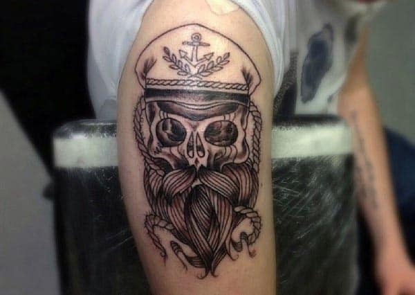 Black and grey tattoo of a bearded skull wearing a captain’s hat with an anchor emblem, detailed with bold lines and shading
