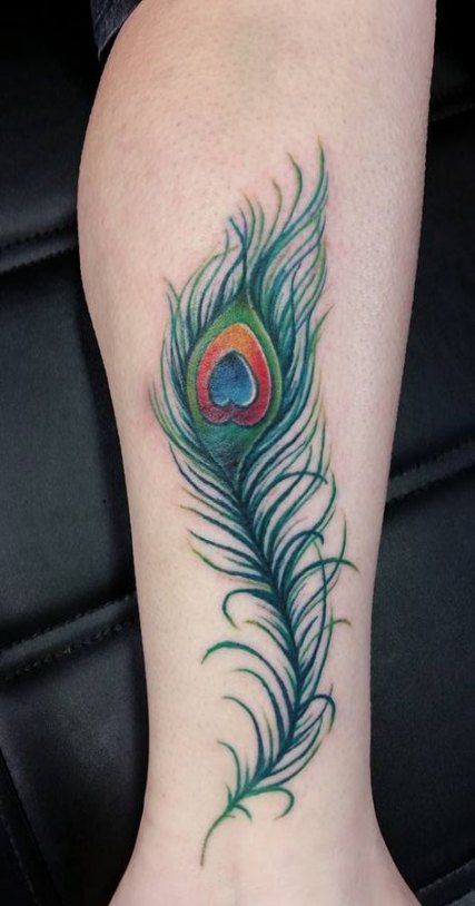 Colorful peacock feather tattoo on the leg, featuring rich green, blue, and gold hues with intricate shading and fine line details.