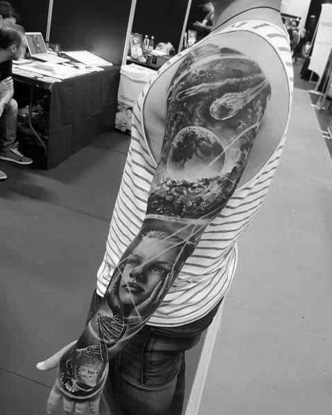 Black and grey full-sleeve tattoo featuring a cosmic theme with a planet, meteor, landscape, and a realistic female portrait for a surreal design.