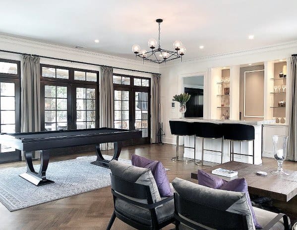Contemporary billiard room with sleek black pool table, bar area, and floor-to-ceiling windows.