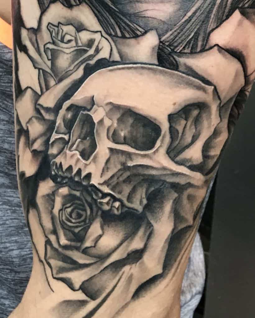 Black and grey tattoo of a realistic skull with roses, featuring deep shading and intricate details for a bold and dramatic sleeve design.