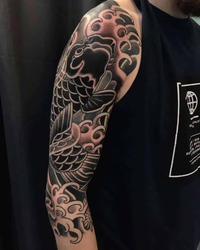 Arm with a detailed black and gray koi fish tattoo, surrounded by waves and clouds