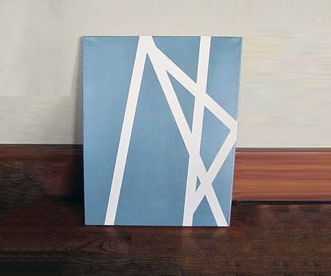 Simple blue canvas art with white geometric lines leaning against a wall.