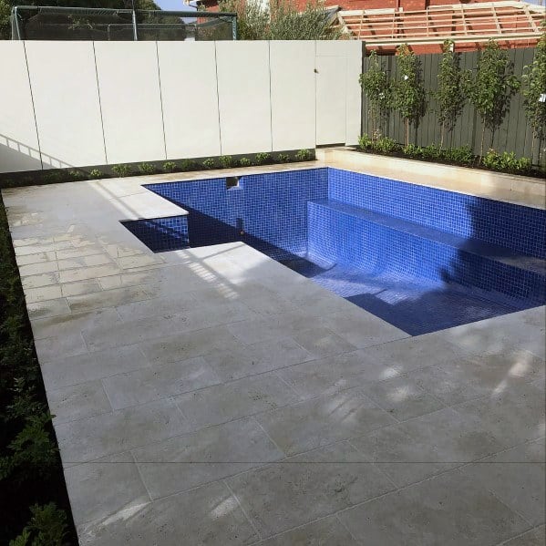 Empty pool with blue mosaic tiles, surrounded by a light stone deck and modern garden accents.