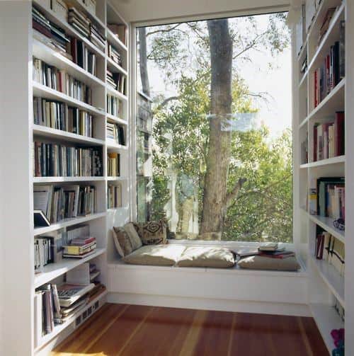 Cozy reading nook with bookshelves and a window seat overlooking a tree outside