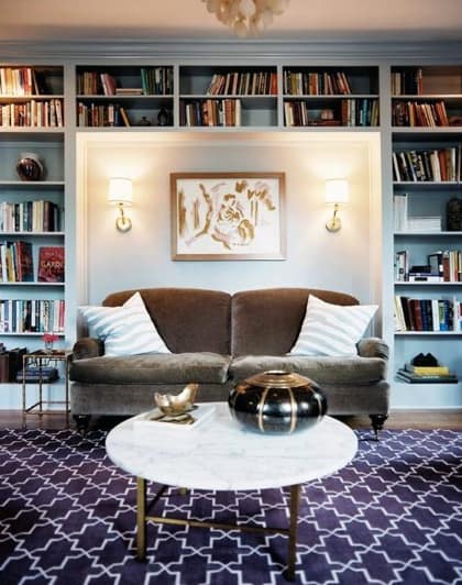 Cozy living room with a brown sofa, bookshelves, a coffee table, and wall sconces