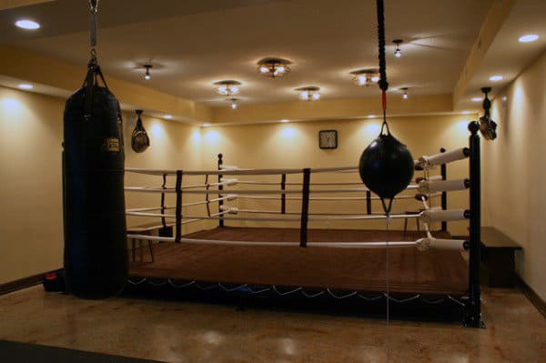 A dimly lit boxing gym feels like home with a boxing ring and hanging punching bags