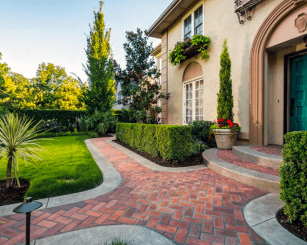 Curved brick walkway leading to a green front door, flanked by neatly trimmed hedges and potted plants, creating an inviting entrance