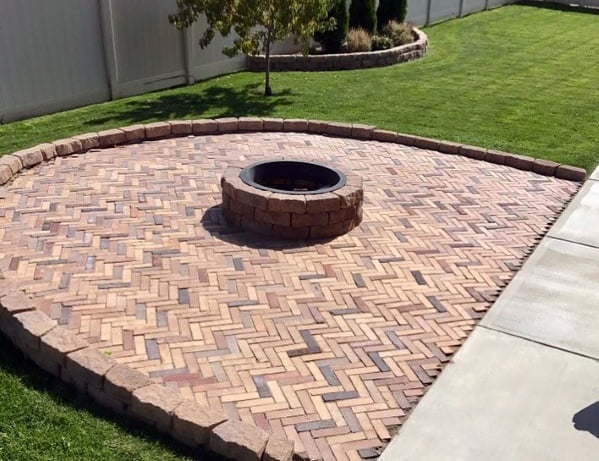 Brick patio with a cozy fire pit surrounded by lush grass in the backyard