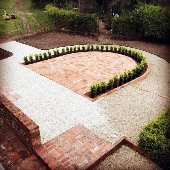 Brick patio with adjacent gravel path and newly planted small bushes