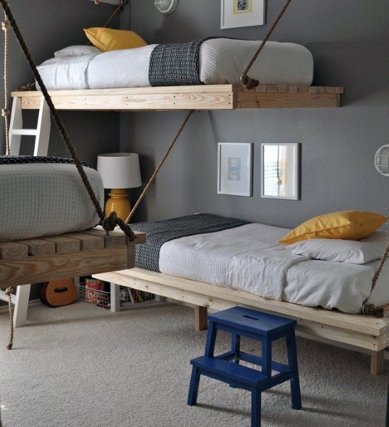 Room with two wooden hanging bunk beds, gray walls, and a blue stool, yellow pillows add a pop of color
