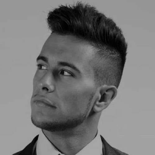 A man with short dark hair, styled upward, gazes to his left