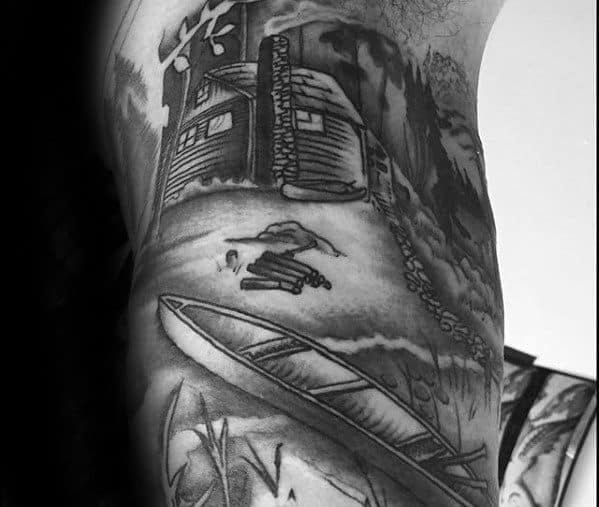 Alt text: Black and grey tattoo featuring a canoe near a log cabin surrounded by trees, with a rustic and peaceful wilderness scene.