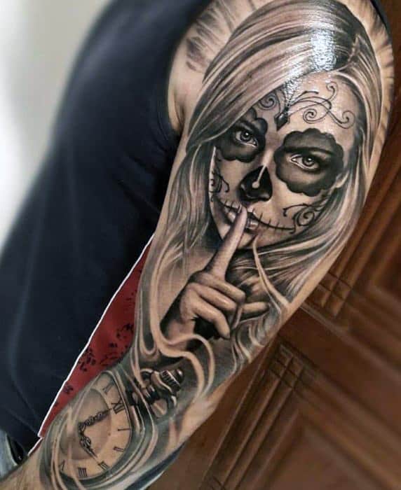La Catrina tattoo of a woman with sugar skull makeup, long flowing hair, a finger to her lips, and a pocket watch below in black and grey.