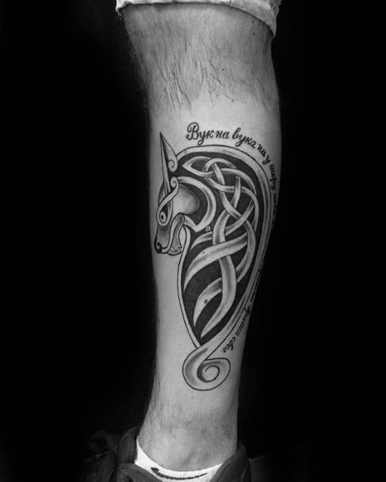 Celtic wolf tattoo on calf with elongated knotwork forming a sleek wolf head and Slavic script curved around the design.