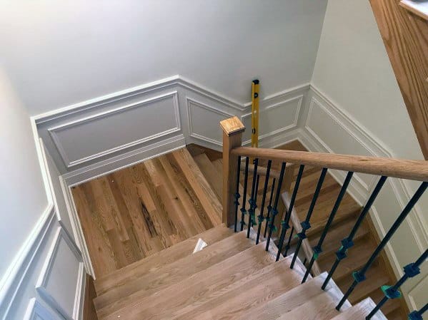 Stylish staircase with light wood steps, white chair rail molding, and black iron spindles for a modern touch