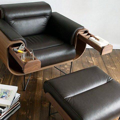 Black leather armchair with pull-out arm storage compartments and matching footrest on wooden flooring.