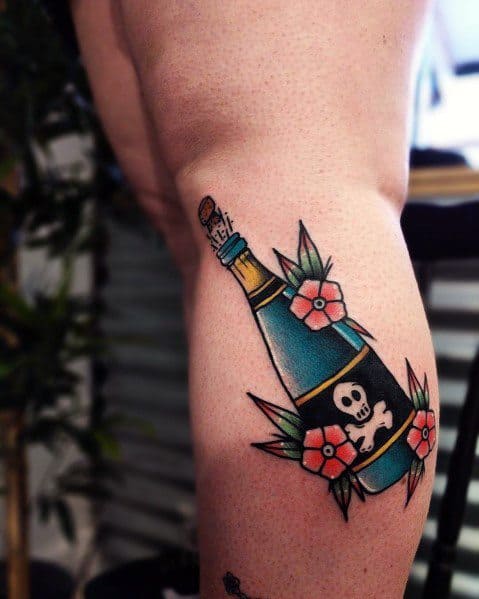 Tattoo of a champagne bottle with a cork, a skull, and red flowers on a person's leg.