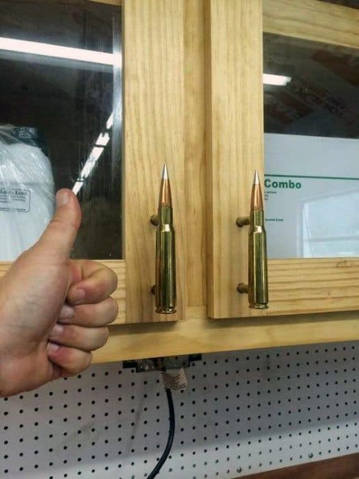Thumbs up next to cabinet handles made from bullets, mounted on wooden cabinet doors