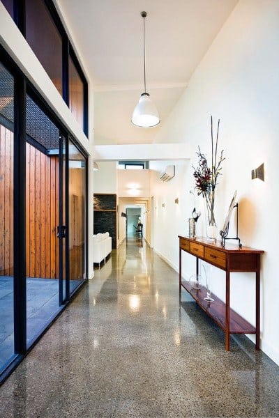 Modern hallway with sleek concrete floor, wooden console table, vase with branches, and large glass doors