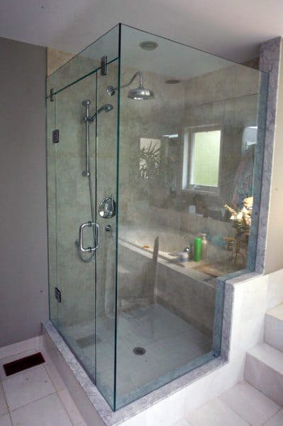 A modern corner glass shower with steps leading up, featuring a built-in bench and rain showerhead