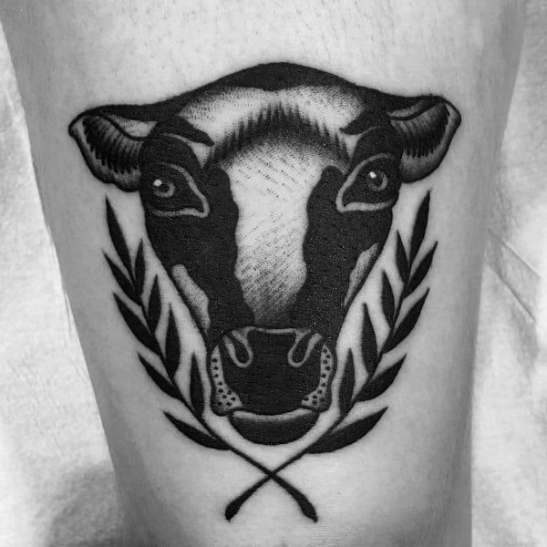 Bold blackwork cow head tattoo with symmetrical laurel leaves, combining traditional and minimal styles for a strong visual impact.
