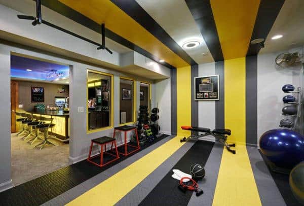 Home gym featuring striped walls, exercise equipment, a pull-up bar, and an adjacent home bar with stools