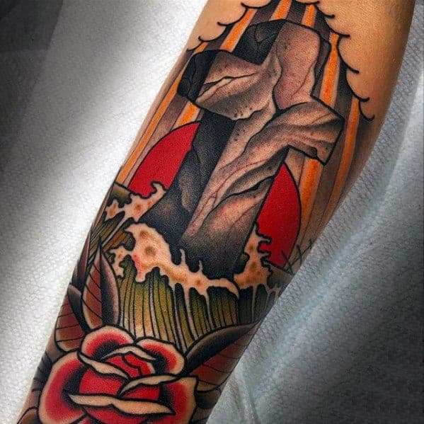 Realistic stone cross tattoo set against a red sun, ocean waves, and clouds, with a traditional red rose at the bottom.
