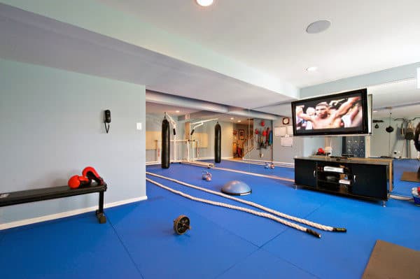 Home gym with blue floor, exercise ropes, bench, TV, weights, mirrors on walls; the perfect home workout space
