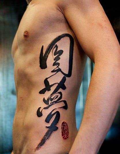 Person's side with black calligraphy tattoo on ribcage and a red stamp-like mark