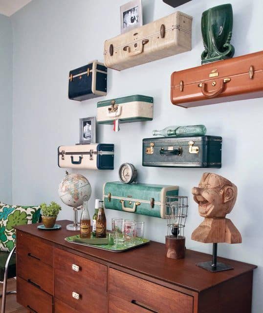 Wall-mounted vintage suitcases serve as shelves above a wooden sideboard with globe and decor items