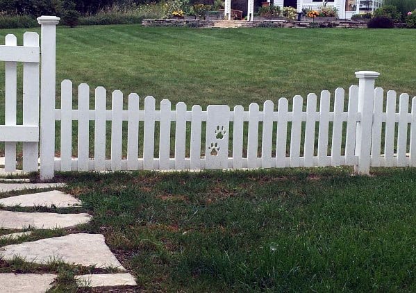 A white fence with cut-out paw prints stands by a grassy area and stone pathway in the foreground