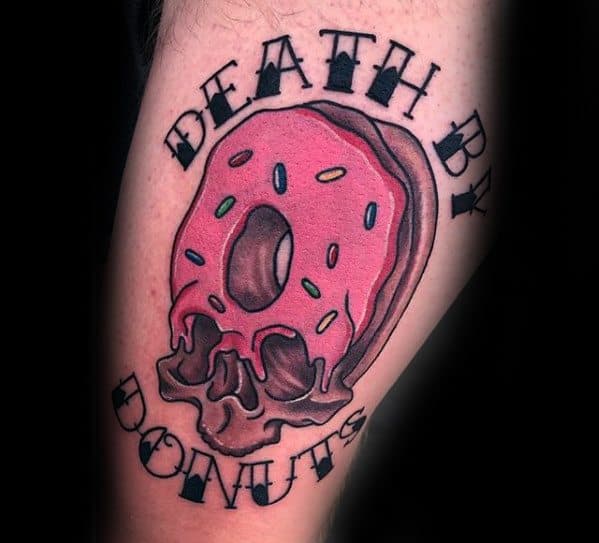 Tattoo of a pink sprinkled donut melting into a skull with the words death by donuts in bold black lettering around it.